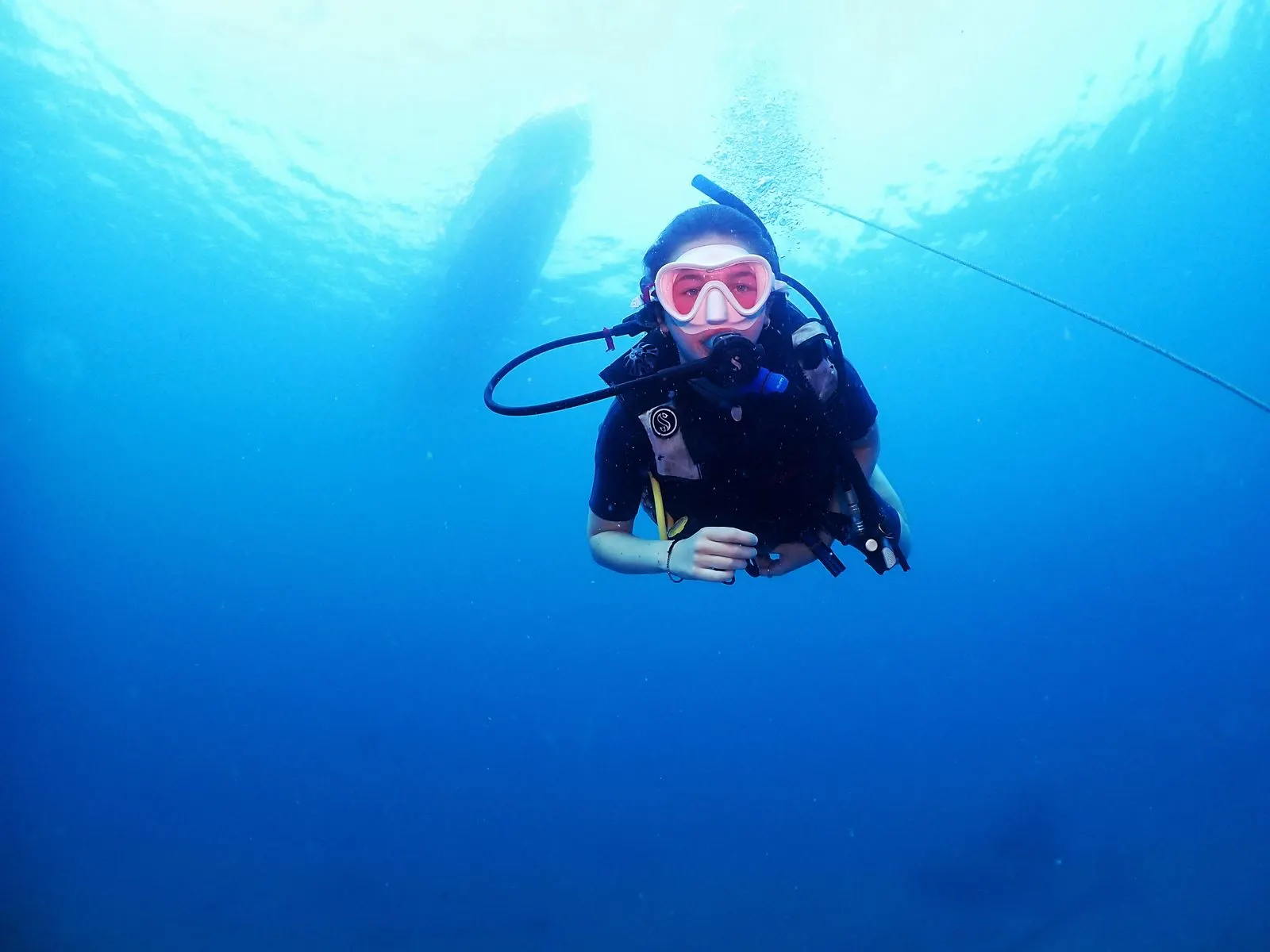 Diver holding perfect horizontal buoyancy in clear blue water with a boat silhouette above