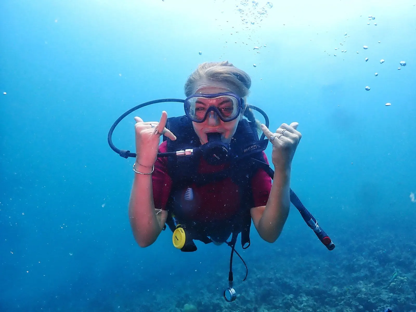 Smiling diver in red shorty giving a shaka while neutrally buoyant above the reef
