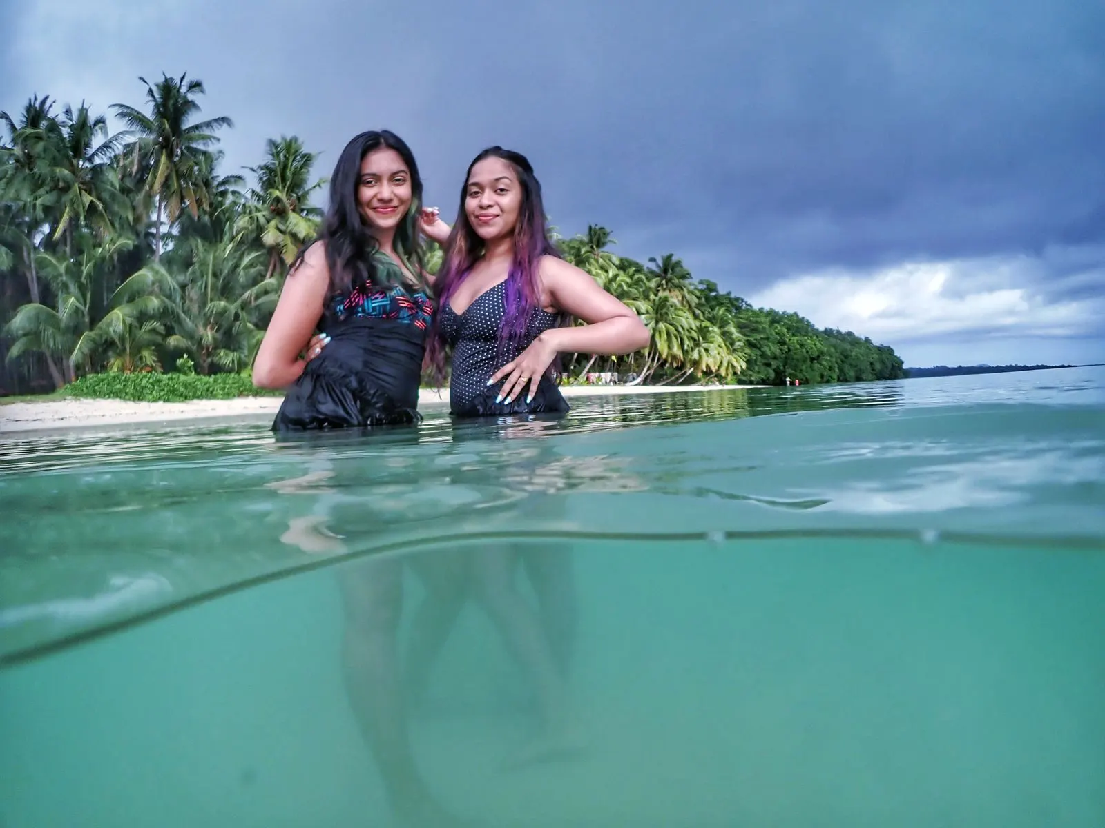 Over-under split shot of two women posing at a tropical shoreline